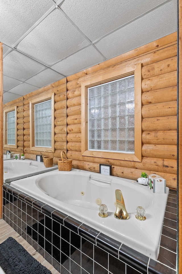 full bath with a drop ceiling, log walls, and a tub with jets