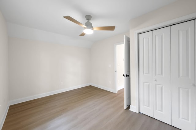 unfurnished bedroom featuring wood finished floors, a ceiling fan, baseboards, vaulted ceiling, and a closet