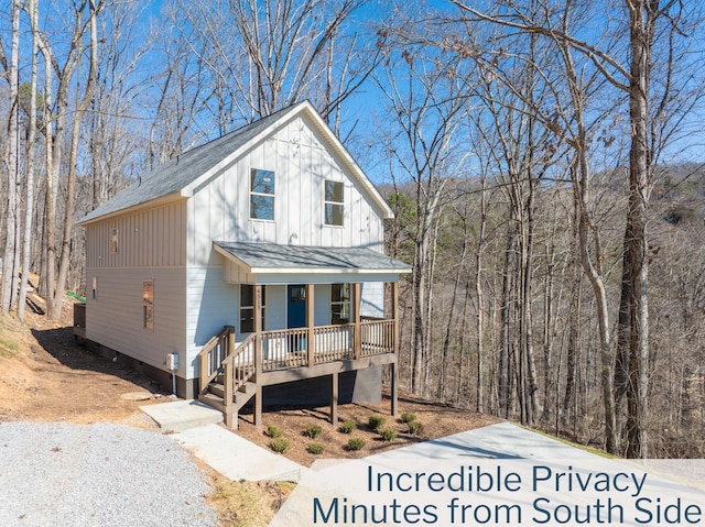 view of front of property featuring board and batten siding, covered porch, roof with shingles, and a wooded view