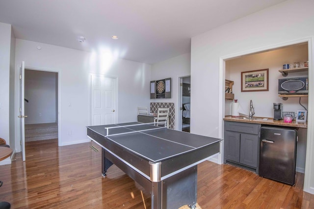recreation room featuring a sink, baseboards, and wood finished floors