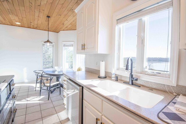 kitchen with light tile patterned floors, stainless steel dishwasher, wood ceiling, white cabinetry, and a sink