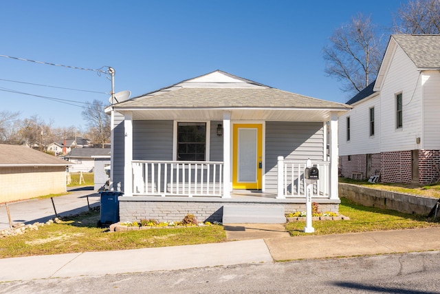 shotgun-style home featuring a shingled roof and a porch