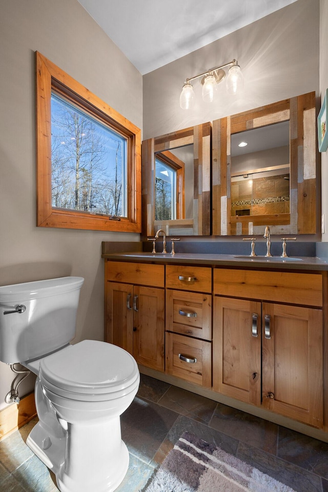 bathroom featuring stone tile flooring, a sink, toilet, and double vanity