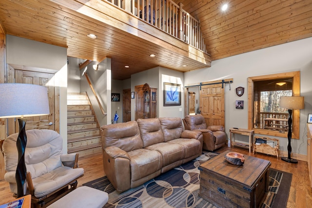 living area with high vaulted ceiling, a barn door, wooden ceiling, wood finished floors, and stairs