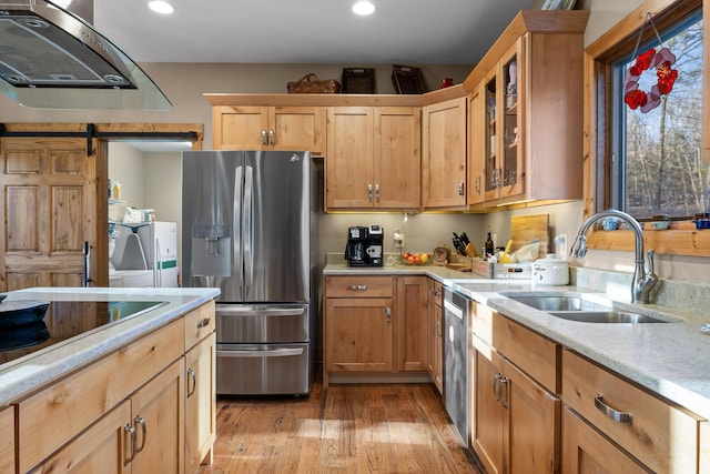 kitchen featuring stainless steel appliances, a barn door, a sink, separate washer and dryer, and exhaust hood