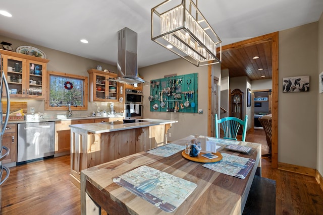 kitchen featuring a center island, island exhaust hood, light countertops, appliances with stainless steel finishes, and wood finished floors