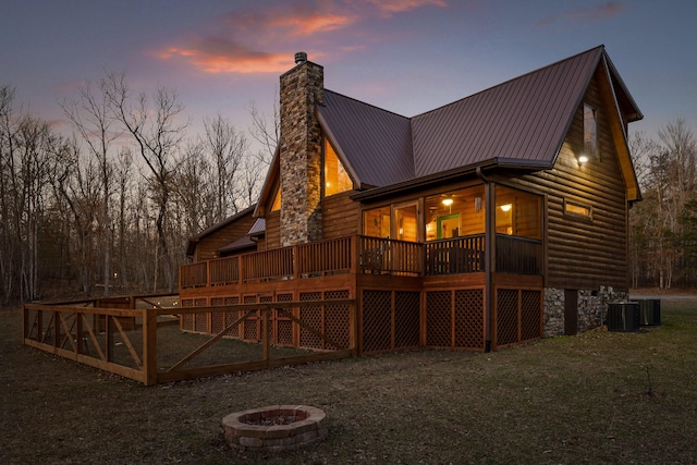 back of house at dusk with metal roof, an outdoor fire pit, central AC, a wooden deck, and a chimney