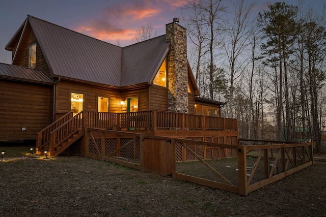 back of house at dusk with a deck, metal roof, stairway, a chimney, and log veneer siding