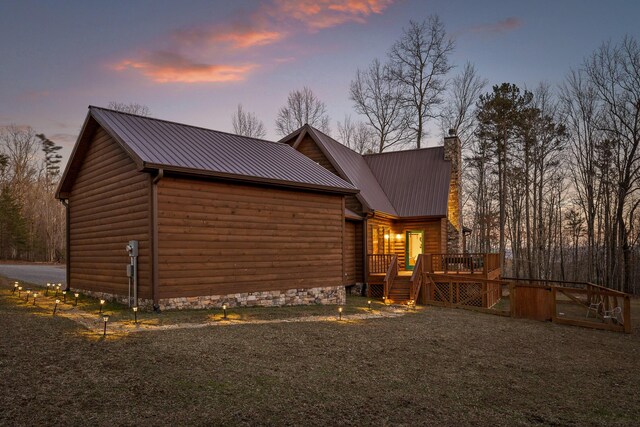 property exterior at dusk with metal roof, a chimney, a deck, and log veneer siding