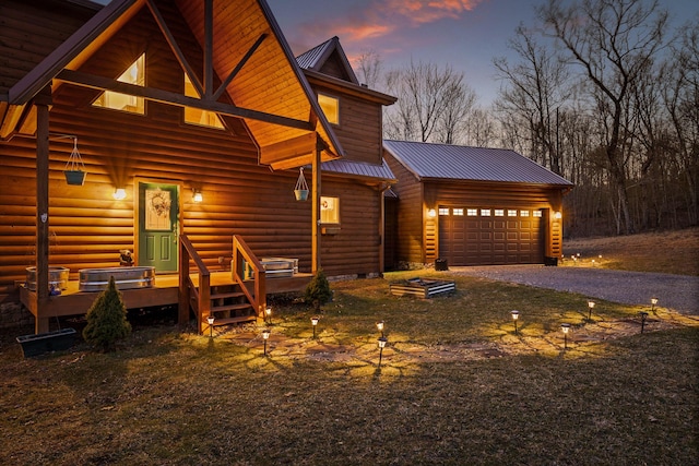 view of front of home with a garage, faux log siding, metal roof, aphalt driveway, and an outbuilding