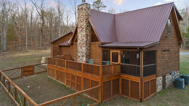 rear view of house featuring a deck, metal roof, a chimney, and a sunroom