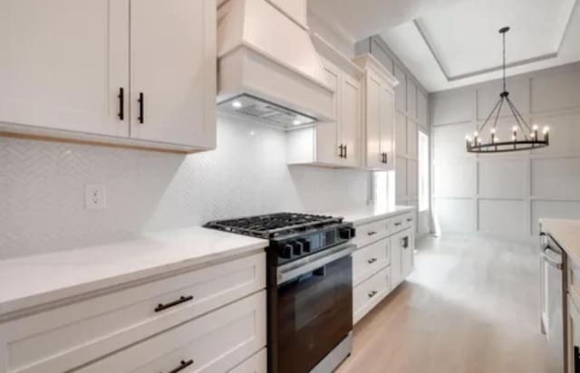 kitchen featuring white cabinetry, custom range hood, light countertops, gas stove, and an inviting chandelier