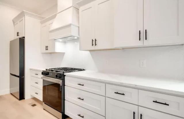 kitchen featuring white cabinets, light wood-style floors, range with gas stovetop, custom exhaust hood, and freestanding refrigerator