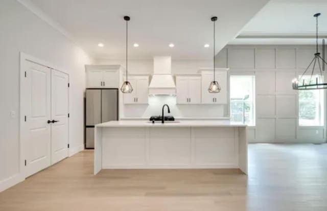 kitchen with a spacious island, freestanding refrigerator, premium range hood, and white cabinetry