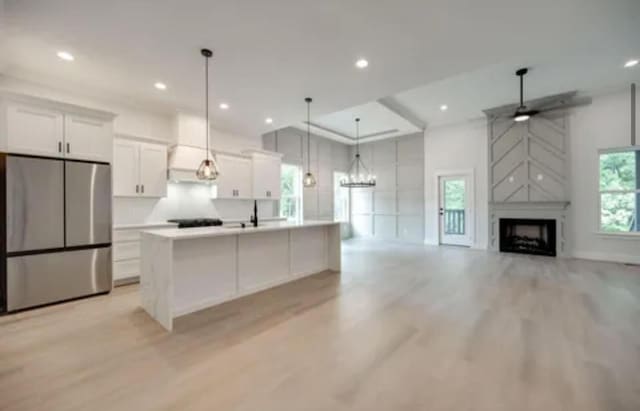 kitchen with white cabinets, a large island, a premium fireplace, freestanding refrigerator, and light countertops