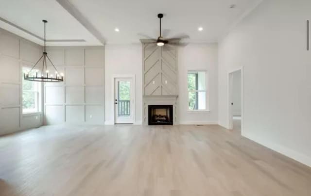 unfurnished living room featuring ceiling fan with notable chandelier, recessed lighting, light wood finished floors, and a premium fireplace