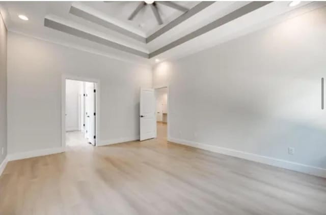 unfurnished room featuring light wood-type flooring, a high ceiling, baseboards, and a raised ceiling