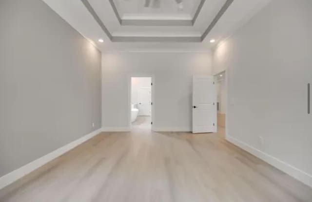 interior space with baseboards, a raised ceiling, light wood-style flooring, ornamental molding, and a high ceiling