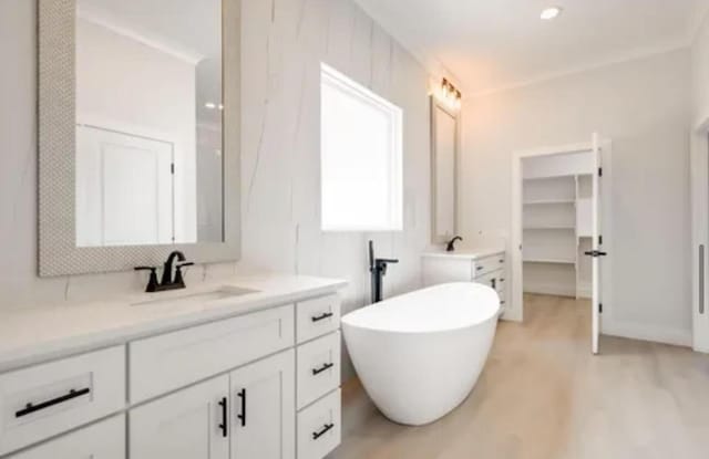 full bathroom with a freestanding bath, wood finished floors, vanity, and a walk in closet