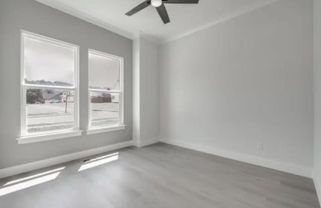 spare room featuring a ceiling fan, baseboards, wood finished floors, and ornamental molding