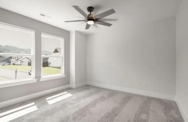 spare room featuring carpet floors, ceiling fan, visible vents, and baseboards