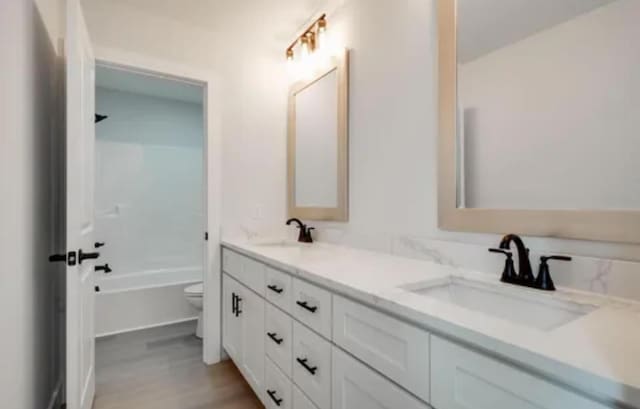 bathroom with double vanity, wood finished floors, a sink, and toilet