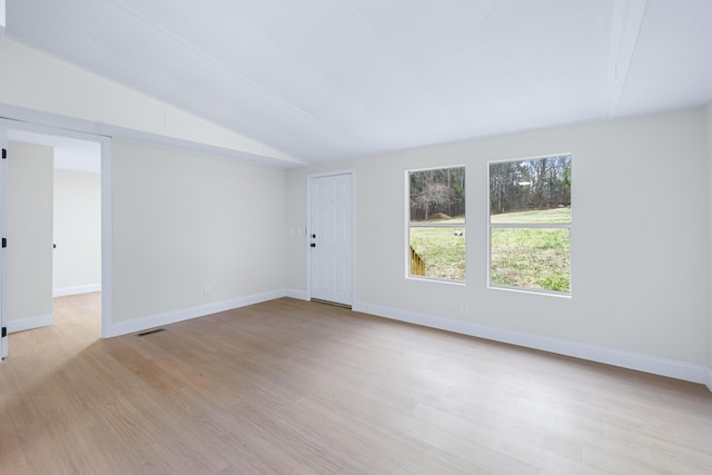 empty room with lofted ceiling, visible vents, light wood-style flooring, and baseboards