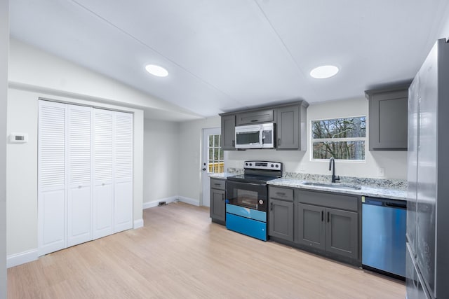 kitchen featuring light stone counters, a sink, light wood-style floors, vaulted ceiling, and appliances with stainless steel finishes