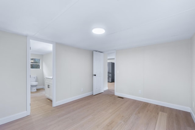 unfurnished bedroom featuring light wood-type flooring, freestanding refrigerator, visible vents, and baseboards