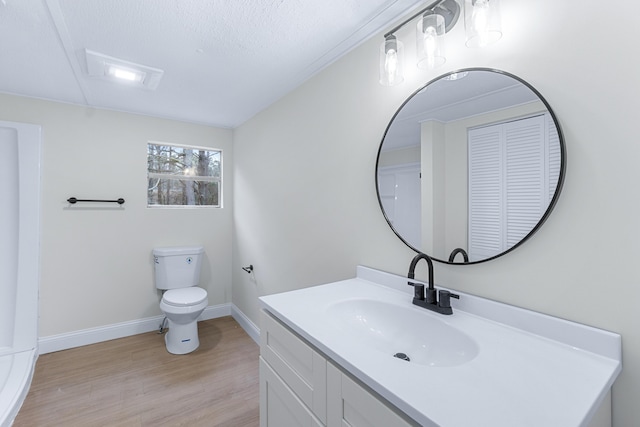 bathroom featuring toilet, a textured ceiling, vanity, wood finished floors, and baseboards