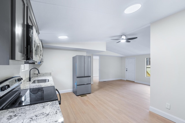 kitchen featuring stainless steel appliances, vaulted ceiling, a sink, ceiling fan, and light wood-type flooring