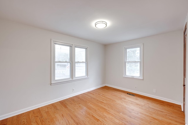 spare room with light wood-style flooring, visible vents, and baseboards