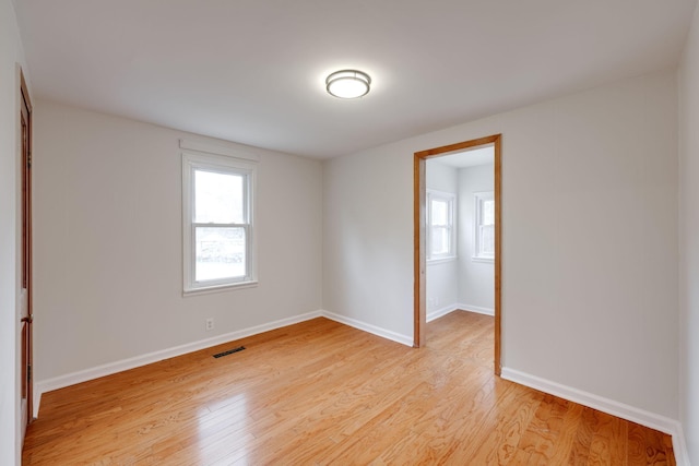 empty room featuring a wealth of natural light, visible vents, light wood-style flooring, and baseboards