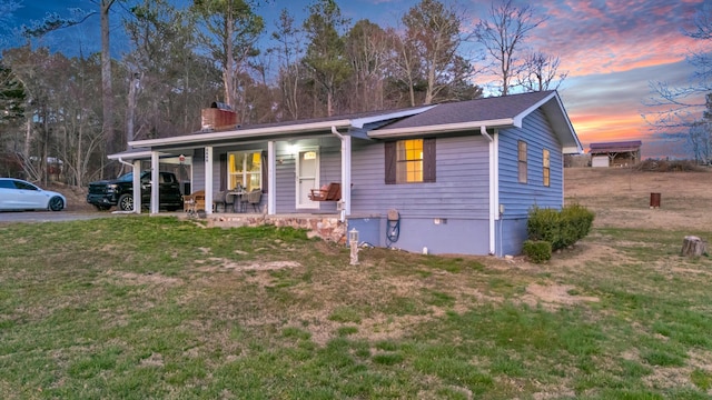 view of front of property with driveway, a chimney, a porch, and a lawn