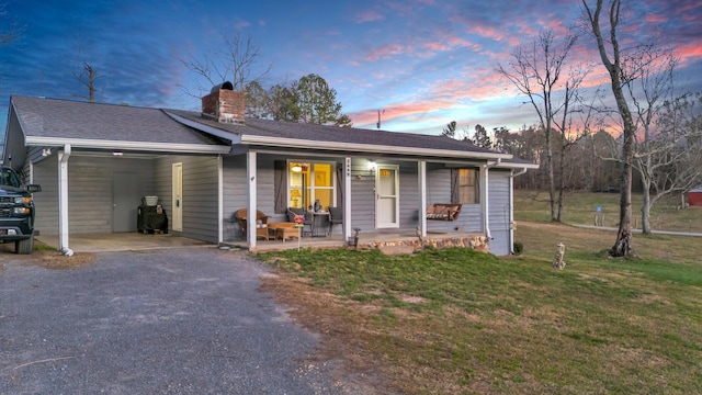 single story home with a chimney, a porch, a lawn, a carport, and driveway