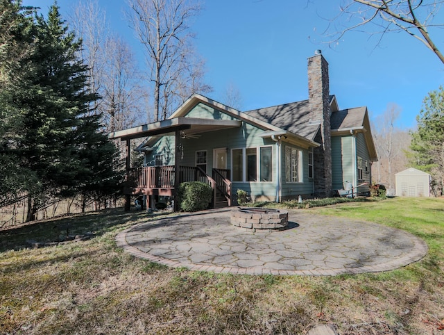 back of property featuring a patio, an outdoor fire pit, an outdoor structure, a yard, and a chimney