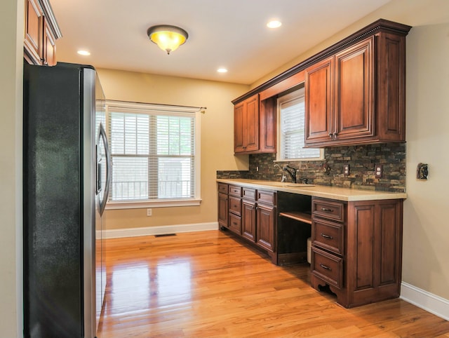 kitchen with baseboards, decorative backsplash, freestanding refrigerator, light countertops, and light wood-style floors