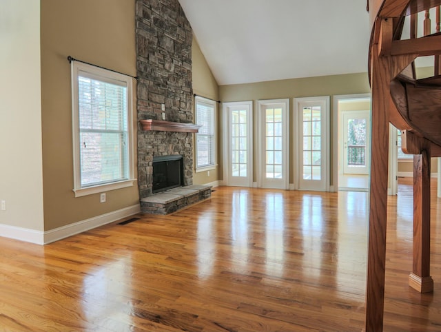 unfurnished living room with high vaulted ceiling, a stone fireplace, wood finished floors, visible vents, and baseboards