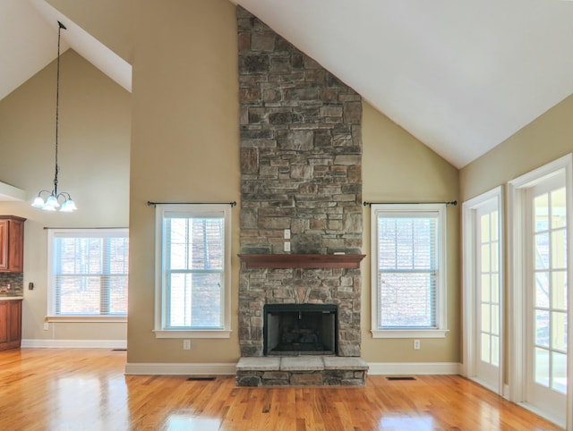 unfurnished living room featuring lofted ceiling, a stone fireplace, light wood-style flooring, visible vents, and an inviting chandelier