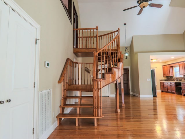 stairway with visible vents, a high ceiling, ceiling fan, wood finished floors, and baseboards