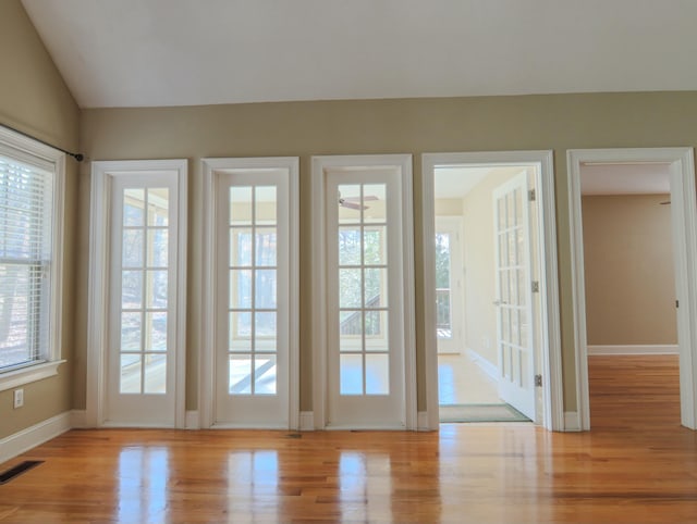 doorway to outside with lofted ceiling, wood finished floors, visible vents, and baseboards