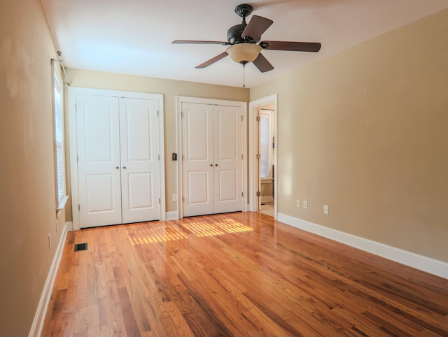 unfurnished bedroom featuring visible vents, baseboards, light wood-style flooring, ceiling fan, and two closets