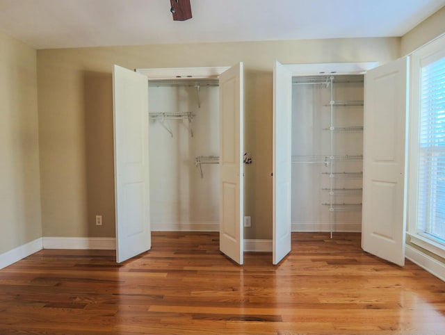 unfurnished bedroom featuring baseboards, wood finished floors, and multiple closets