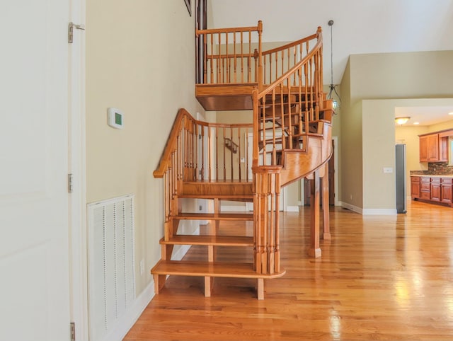 staircase with baseboards, a high ceiling, visible vents, and wood finished floors