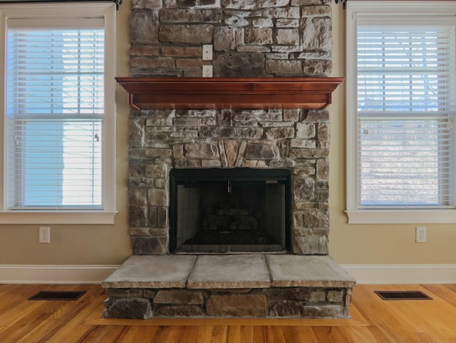 details featuring a stone fireplace, wood finished floors, visible vents, and baseboards