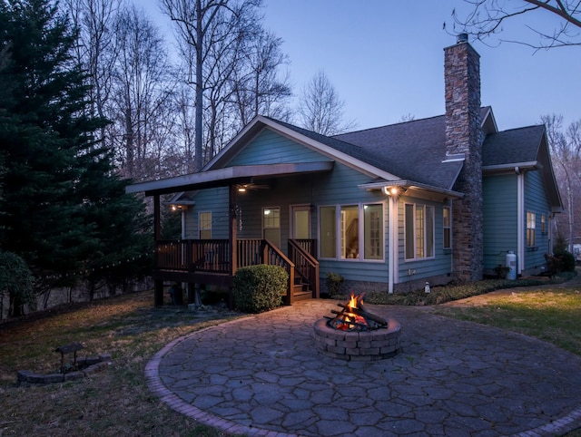 view of front of house featuring a fire pit, ceiling fan, a chimney, roof with shingles, and a patio area