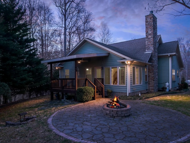 view of front of home with roof with shingles, a patio, a chimney, an outdoor fire pit, and ceiling fan