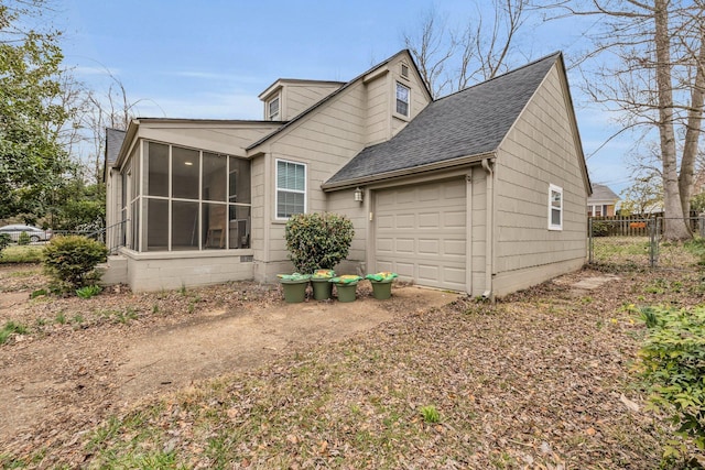 view of side of home featuring a garage, driveway, a shingled roof, a sunroom, and fence