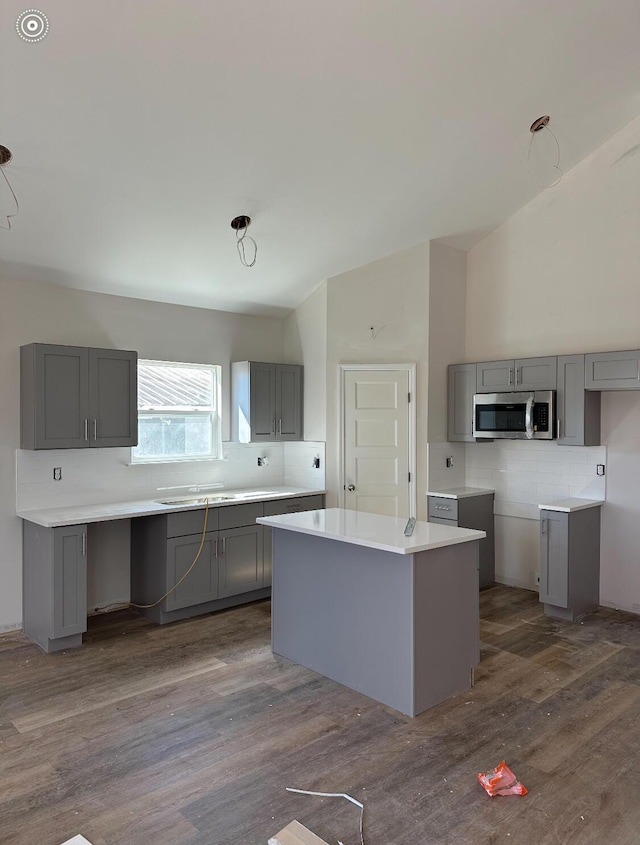 kitchen featuring dark wood finished floors, gray cabinets, stainless steel microwave, decorative backsplash, and vaulted ceiling