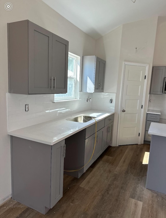 kitchen featuring gray cabinets, light countertops, decorative backsplash, dark wood-type flooring, and a sink